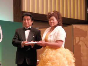 黄色のドレスに身替えた酒井美紀（右）。半田会長（左）とチャリティ金をいわき市へ手渡した（ホテルオークラ東京）。